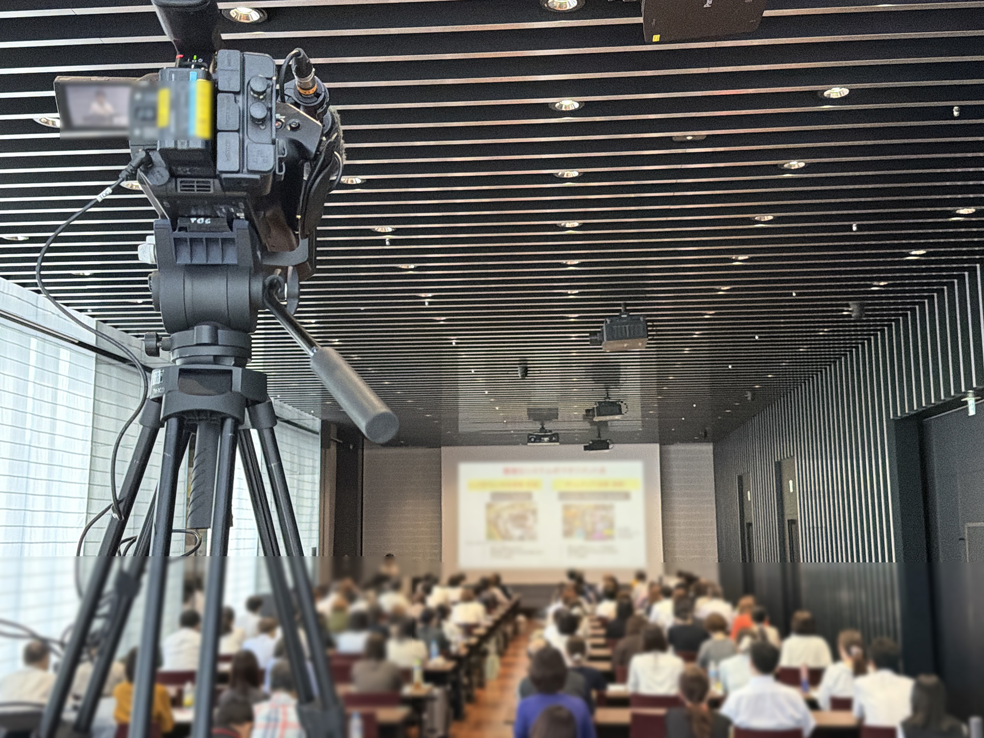 参加者が着席したセミナー会場で三脚に据えた業務用カメラによる撮影風景